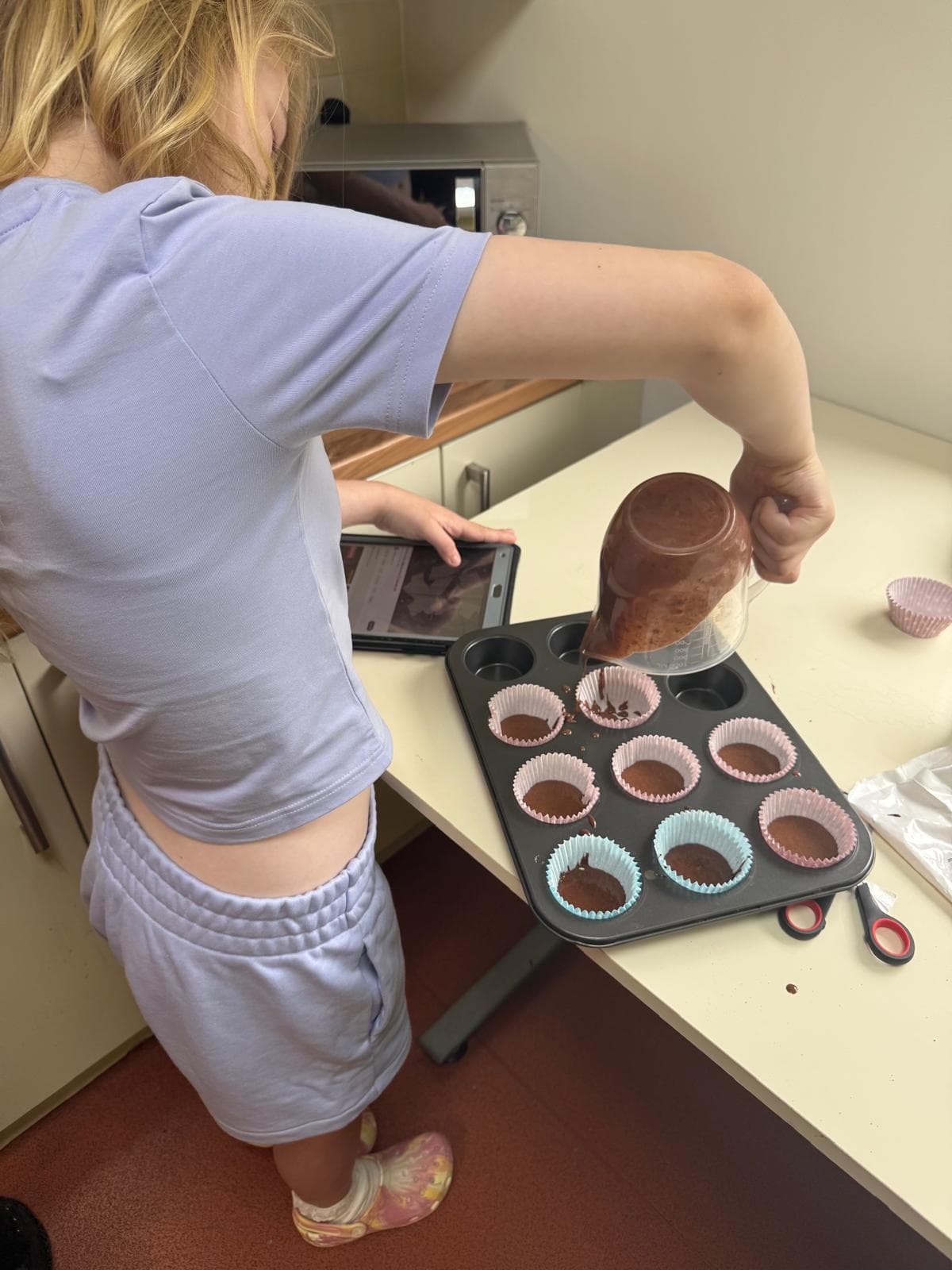 Child carefully pouring batter into cupcake cases during a baking session