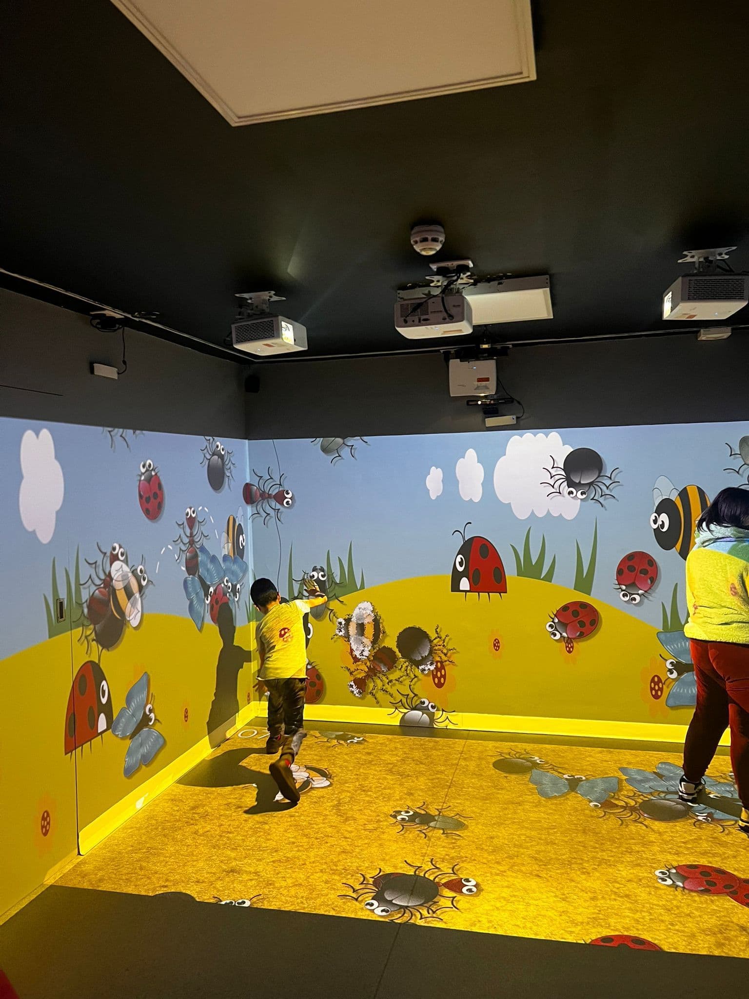 Child interacting with immersive bug-themed projection on walls and floor