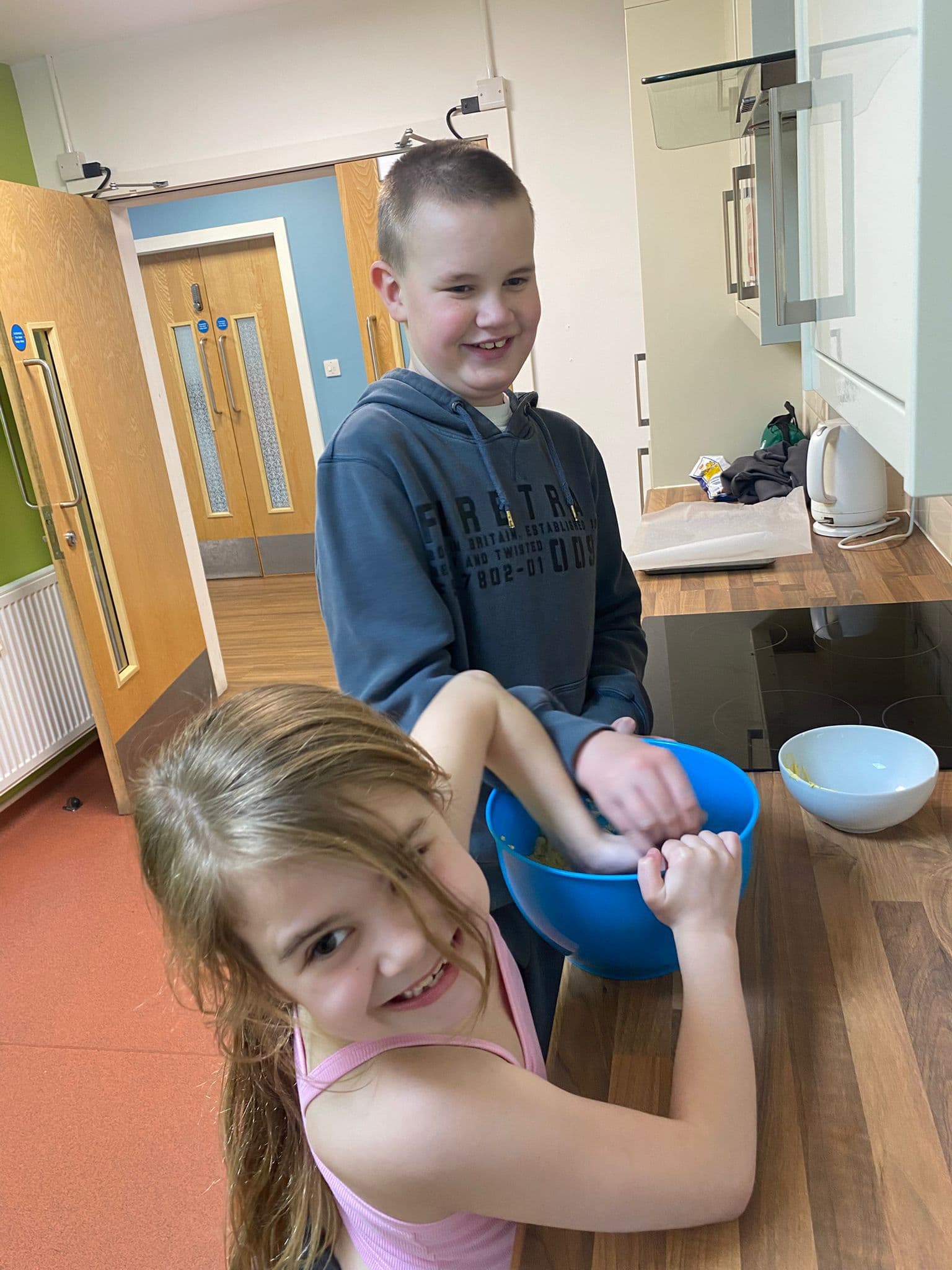 Two children smiling while cooking together in the kitchen